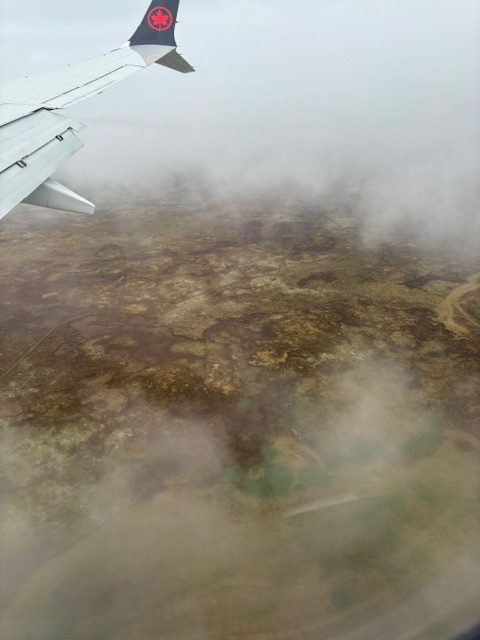 Mystical aerial view of Iceland taken from my window seat. The view of the brown and yellow ground partially hidden in a fog of clouds. 